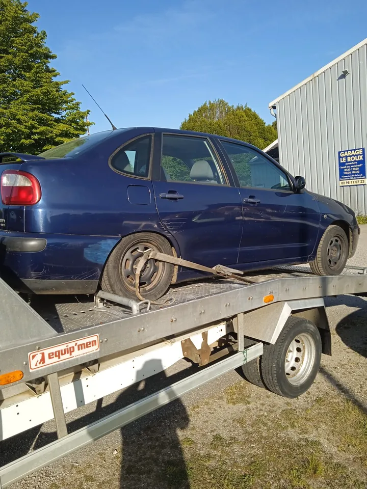Berline rayée sur un plateau avec une sangle fixée près de la roue arrière.
