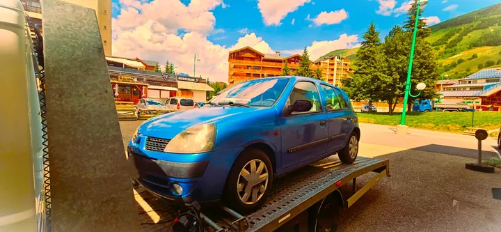 Renault Clio chargée sur un camion-plateau en bord de route.