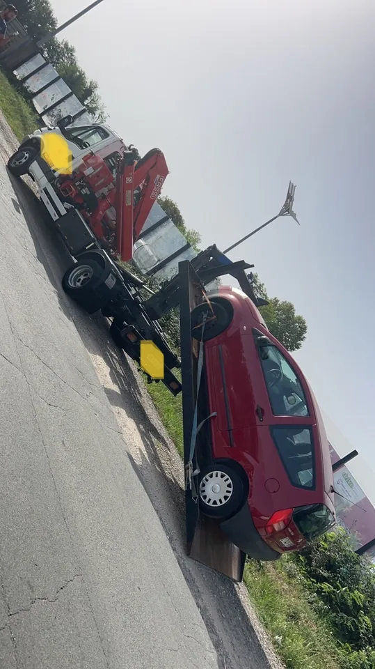 Break rouge chargé sur le plateau d’un camion équipé d’une grue.