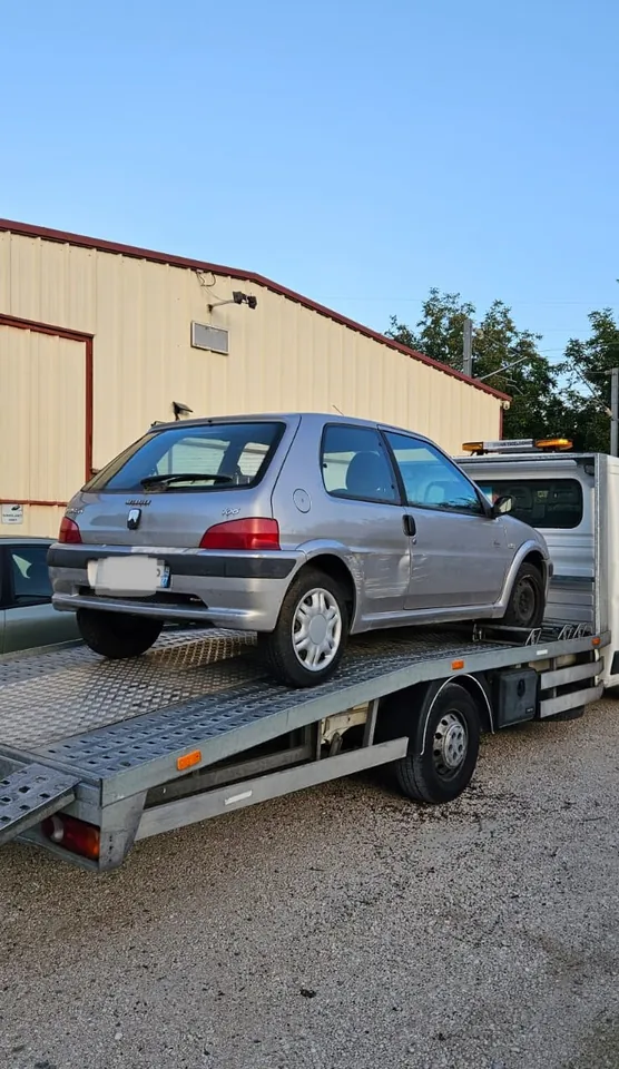 Peugeot 106 sur une dépanneuse devant un bâtiment à bardage.