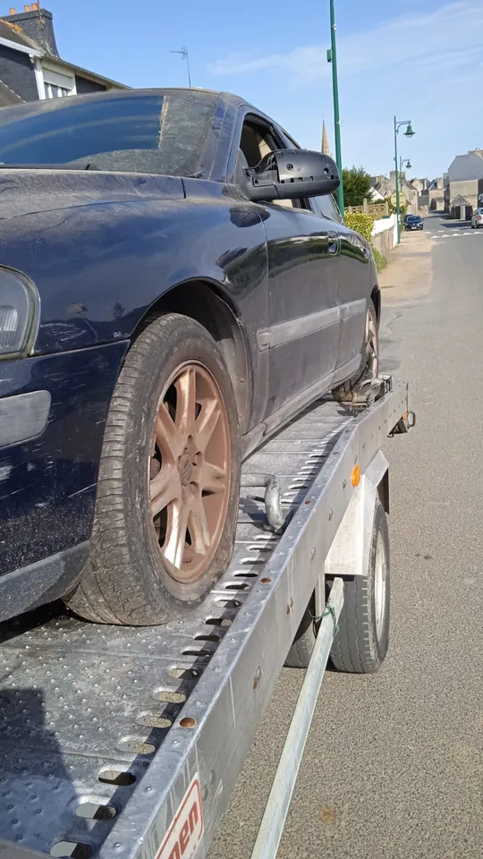 Berline sur une dépanneuse avec un appui métallique derrière une roue avant.