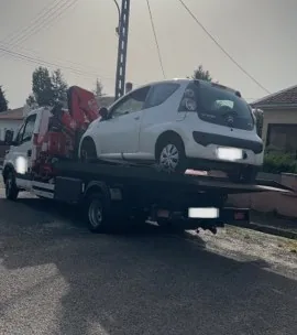 Petite voiture blanche sur le plateau d’un camion à grue rouge.