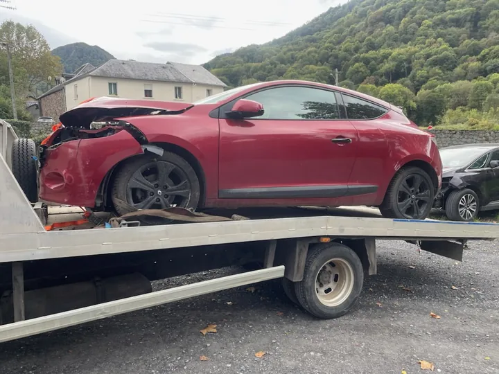 Coupé rouge au capot et à l’aile avant déformés sur un camion plateau.