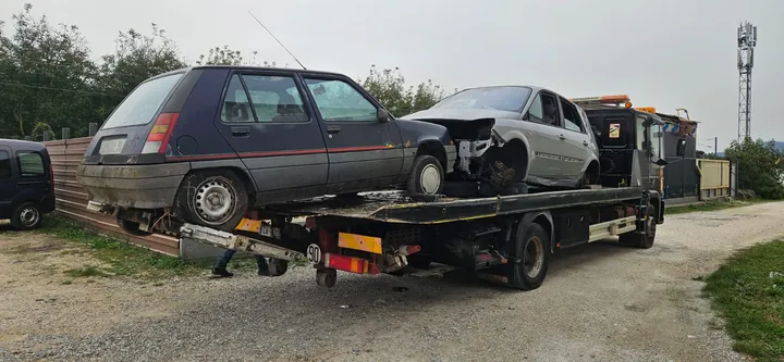 Deux voitures sur un camion plateau, dont une claire à l’avant partiellement démonté.