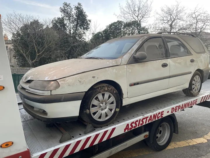 Voiture beige recouverte de poussière sur un camion plateau blanc.