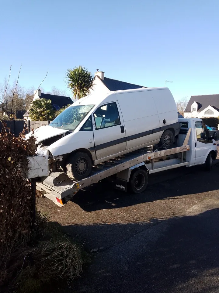 Fourgon blanc à carrosserie fermée chargé sur un camion plateau.