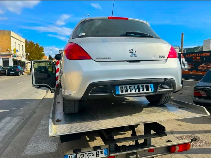 Arrière d’une voiture claire à cinq portes chargée sur un camion plateau.