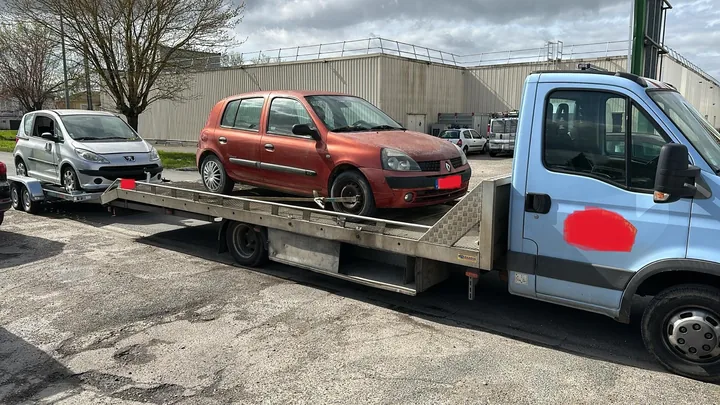 Deux petites voitures, rouge et claire, chargées l’une derrière l’autre sur un long plateau.