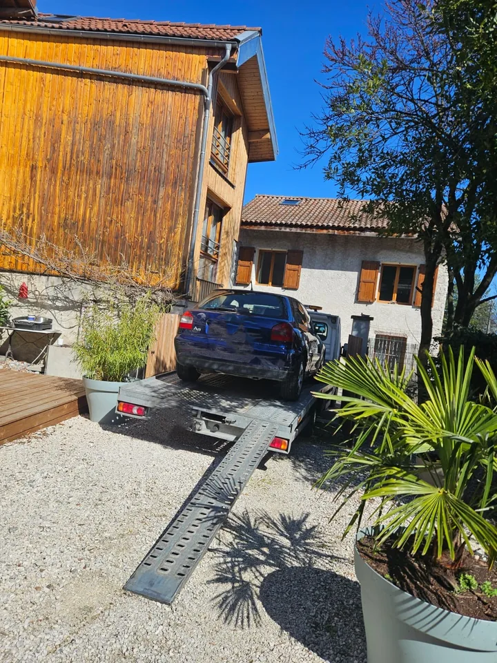 Voiture sombre sur un plateau avec rampe déployée dans une cour entre des bâtiments.