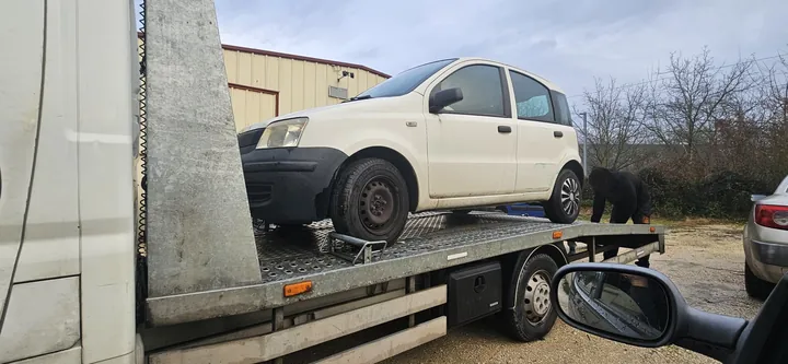 Petite voiture blanche à cinq portes chargée sur le plateau d’un camion.