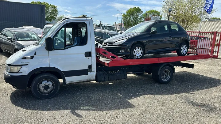 Voiture compacte sombre chargée sur le plateau rouge d’un camion blanc.