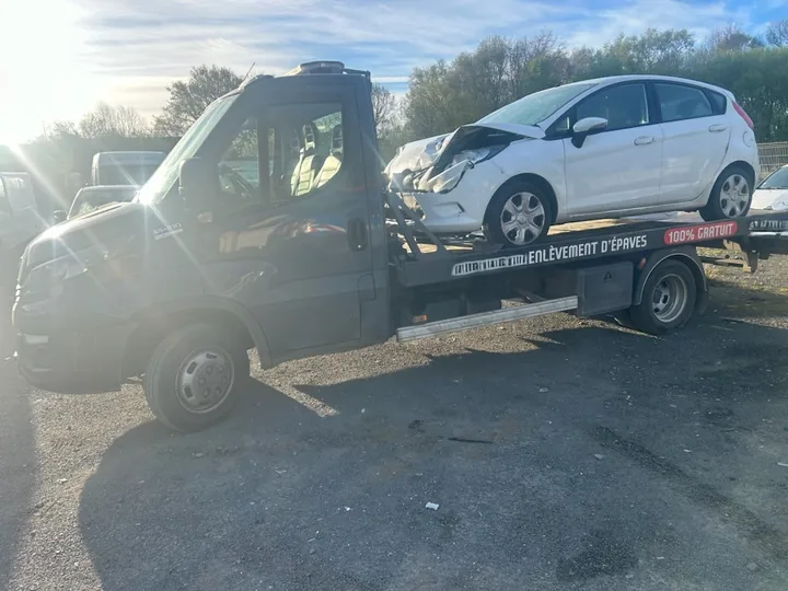 Voiture claire à l’avant déformé sur un camion plateau sombre.