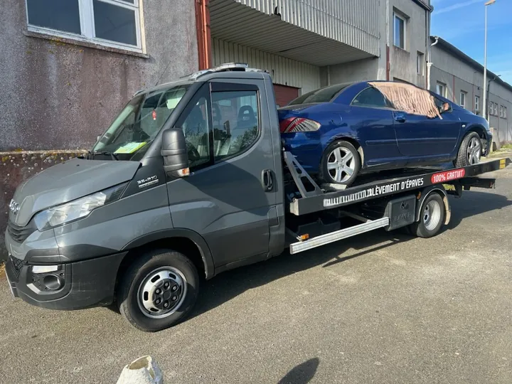 Coupé bleu sur un camion plateau avec une protection couvrant une partie de sa carrosserie.
