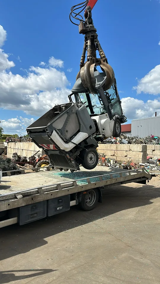 Balayeuse compacte maintenue par une pince au-dessus d’une plateforme de transport.
