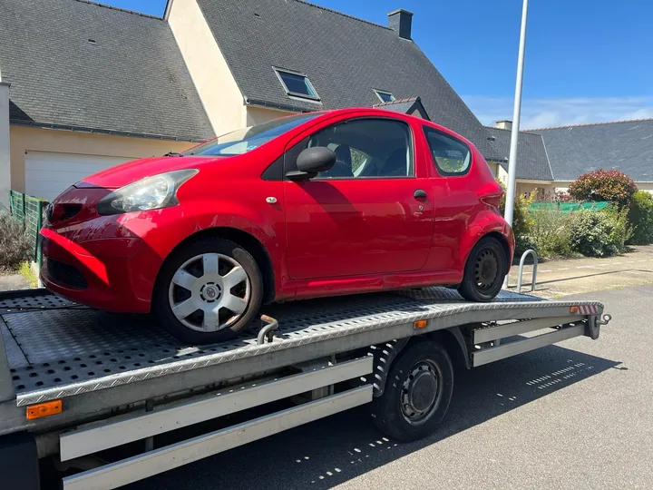 Citadine rouge avec des cales près des roues sur une dépanneuse.