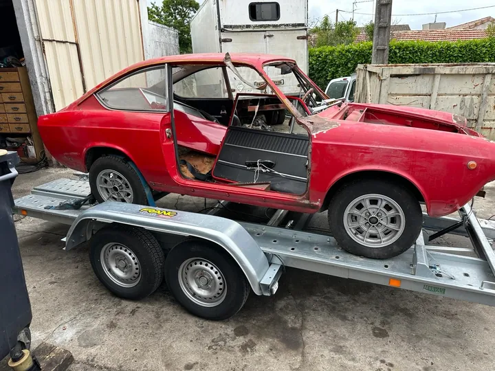 Voiture ancienne sans capot ni pare-brise sur une remorque à deux essieux.