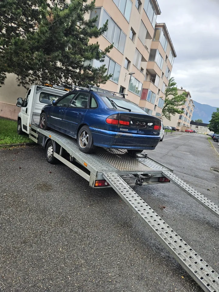 Berline bleue chargée sur un plateau avec deux rampes déployées en rue.