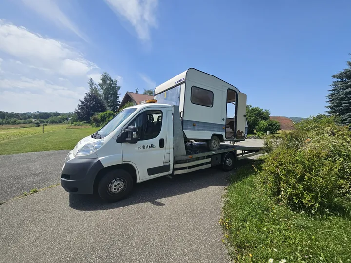 Petite caravane chargée sur le plateau d’une dépanneuse blanche.