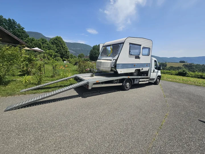 Caravane claire sur une dépanneuse avec deux rampes abaissées sur la route.