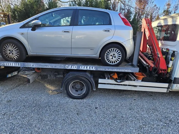 Citadine claire chargée sur un plateau près d’une grue rouge repliée.