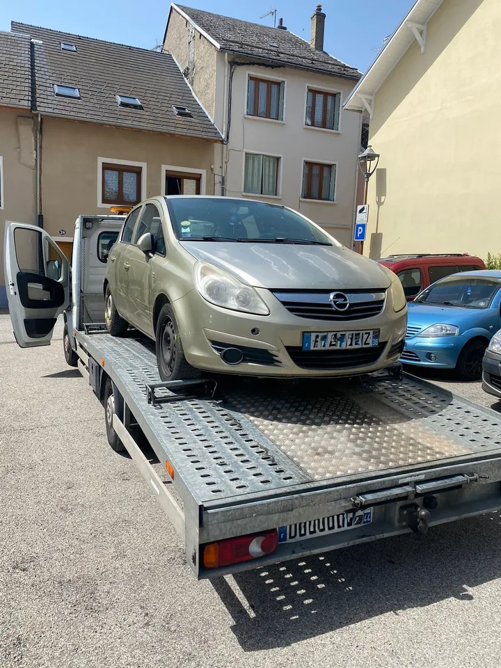 Citadine claire avec des cales aux roues sur une dépanneuse, près de voitures garées.