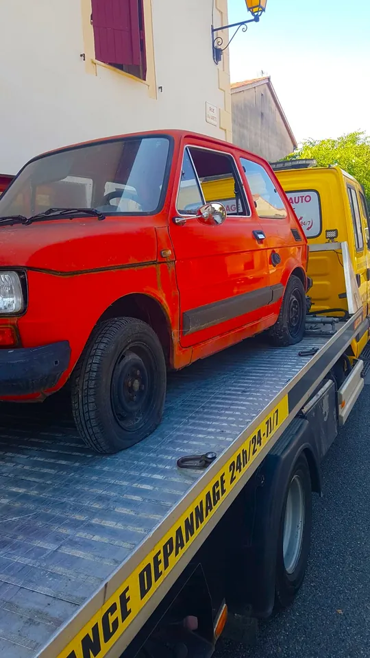 Petite voiture rouge ancienne à bas de caisse marqués sur une dépanneuse.