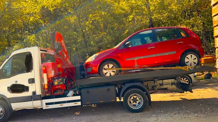 Citadine rouge sur une dépanneuse, devant une grue rouge repliée.