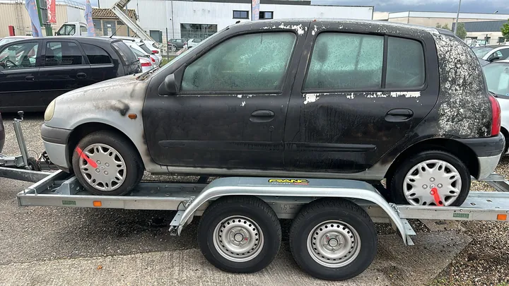 Citadine à peinture altérée avec des sangles aux roues sur une remorque.