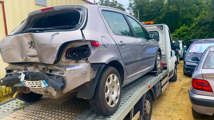 Peugeot 307 au hayon déformé et au pare-chocs arrière absent sur un plateau.