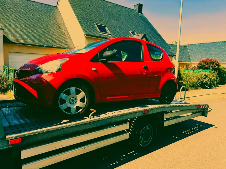 Citadine rouge chargée sur un plateau avec un appui près d’une roue.