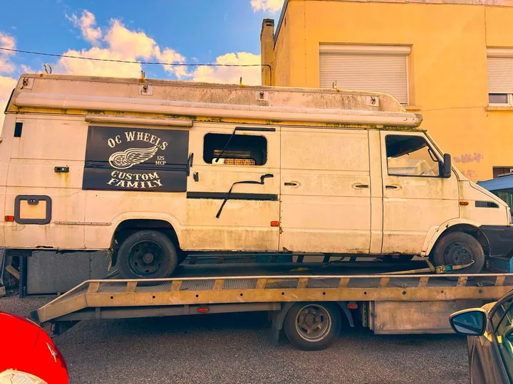 Ancien fourgon blanc à caisse haute et équipements de toit sur un camion plateau.