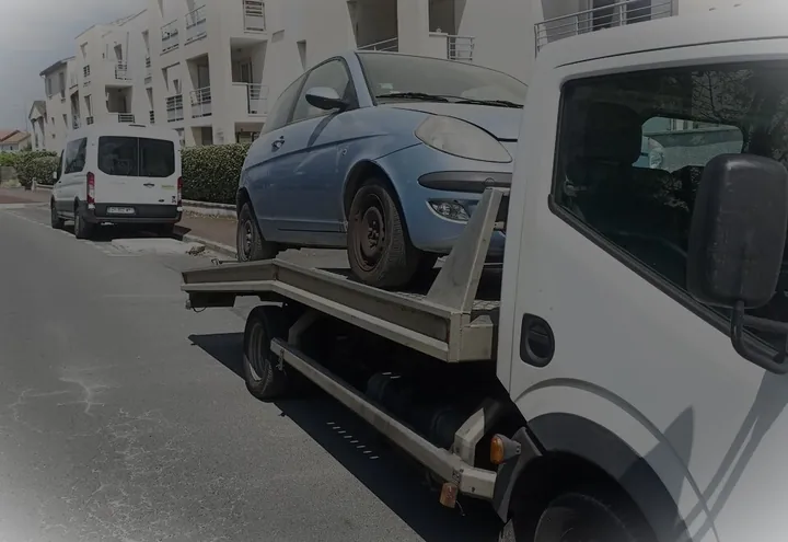 Citadine bleue sur une dépanneuse blanche près d’immeubles et de véhicules garés.