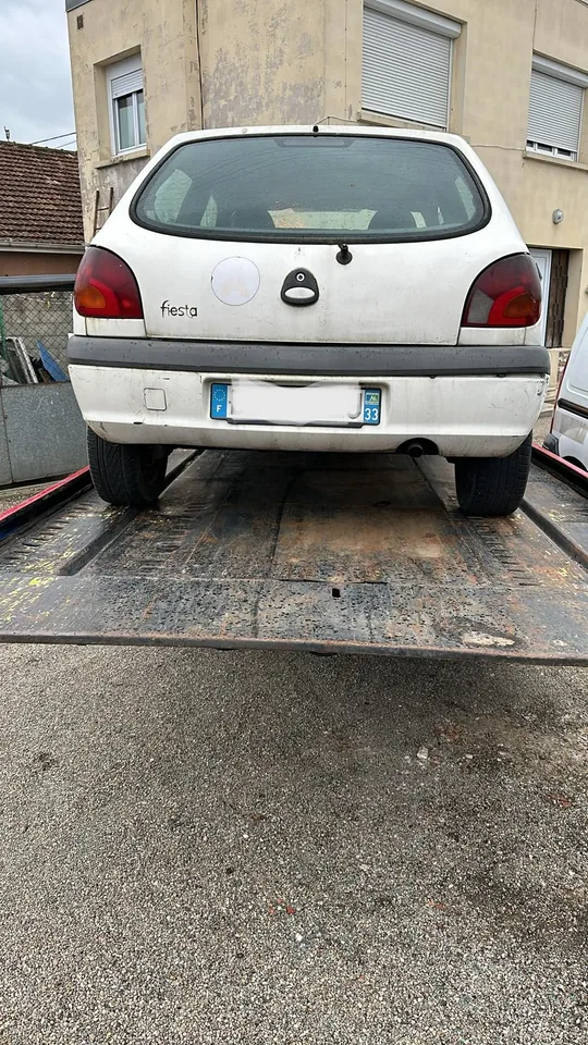 Arrière d’une Ford Fiesta blanche chargée sur un plateau métallique.